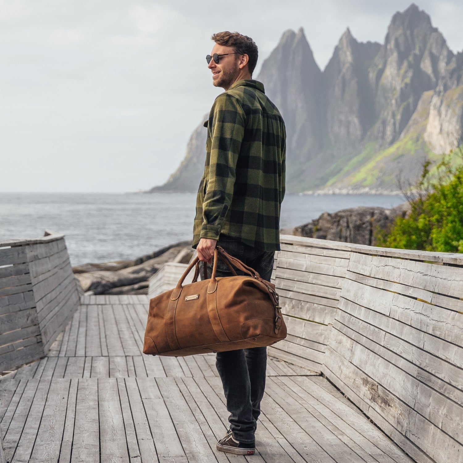 Mann steht vor Bergkulisse am Meer und hat eine handgemachte Leder Reisetasche von DRAKENSBERG in der Hand