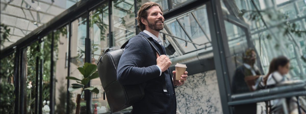 Voyageur avec un sac à dos en cuir noir et un café devant une façade vitrée historique