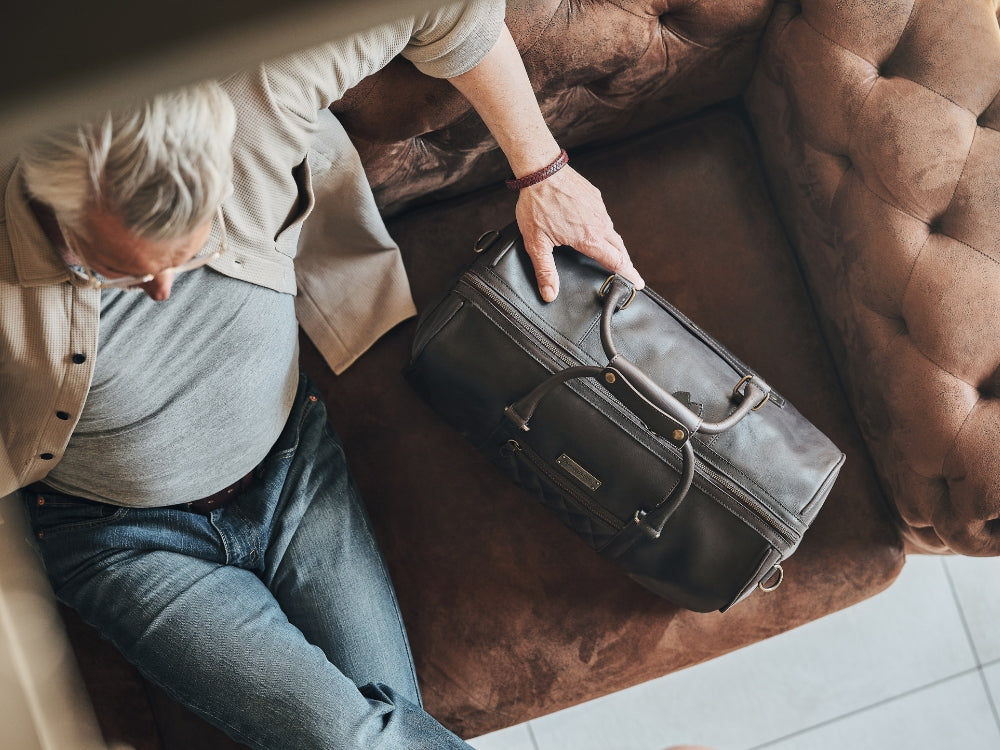 Overhead view of a man with a dark brown leather weekender on a brown Chesterfield sofa