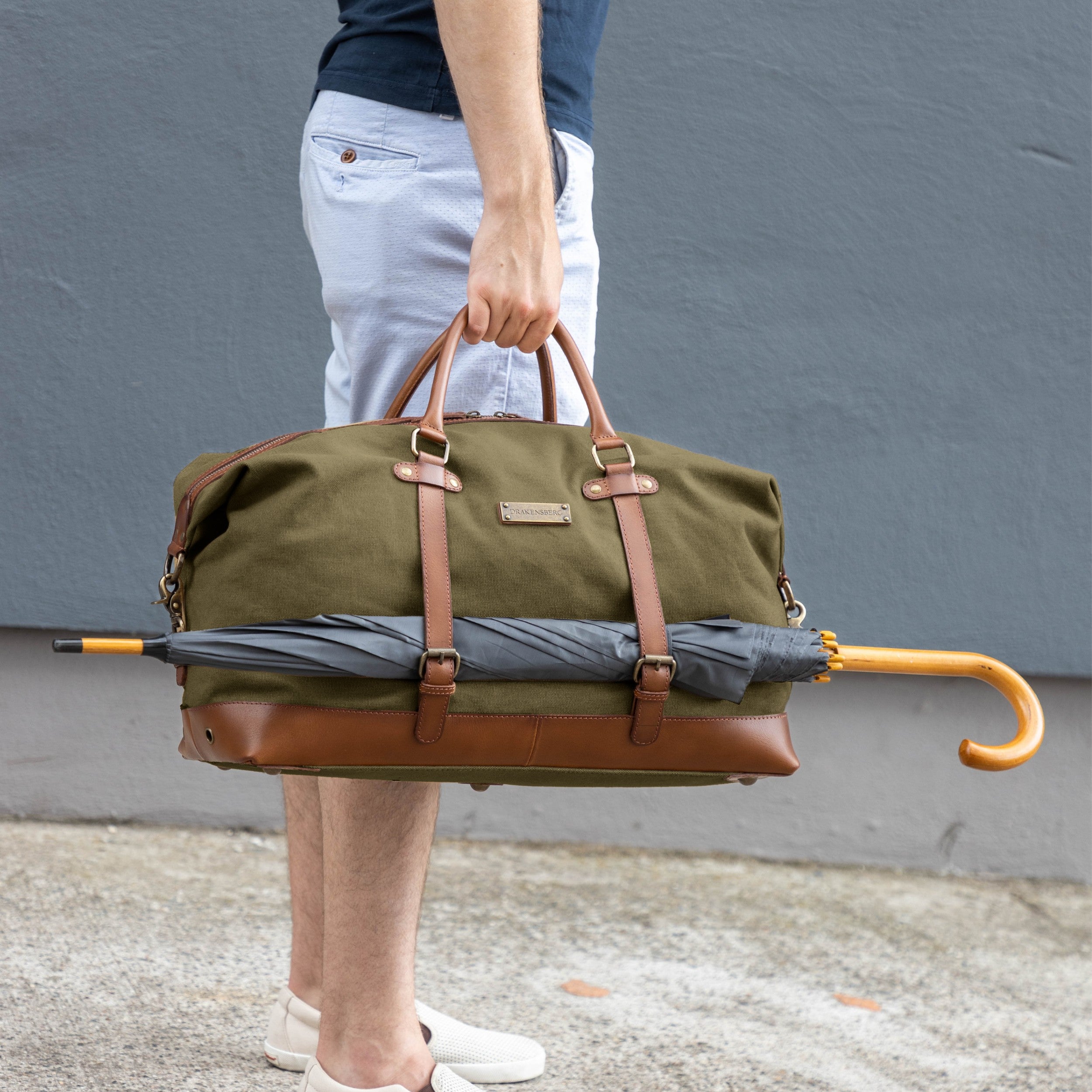 Canvas Weekender Owen Oliv-Grün mit Leder-Elementen - Mann trägt die Sporttasche befüllt und an der Seite ist ein großer Regenschirm befestigt