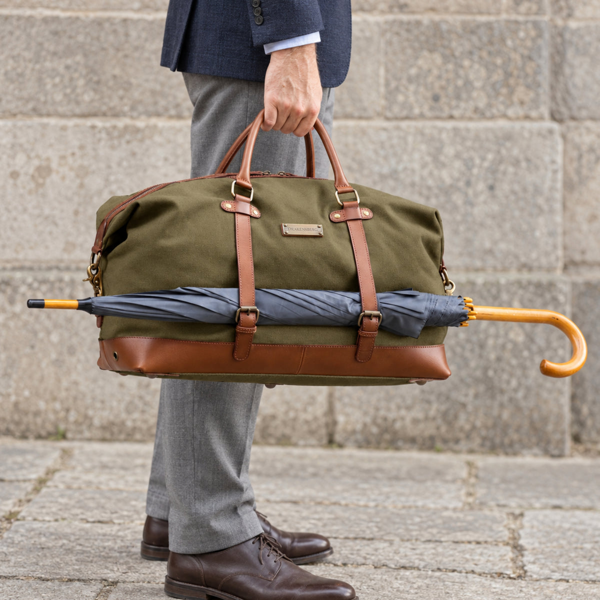 Canvas Weekender Owen Oliv-Grün mit Leder-Elementen - Mann trägt die Sporttasche befüllt und an der Seite ist ein großer Regenschirm befestigt
