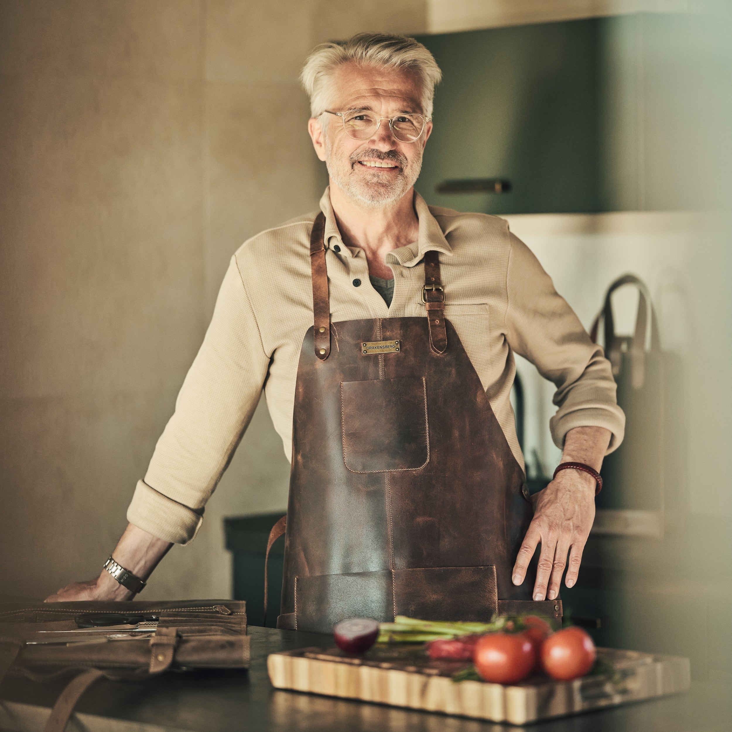 Mann steht in der Küche mit einer Ledergrillschürze von DRAKNSBERG in Dunkelbraun Antiklook
