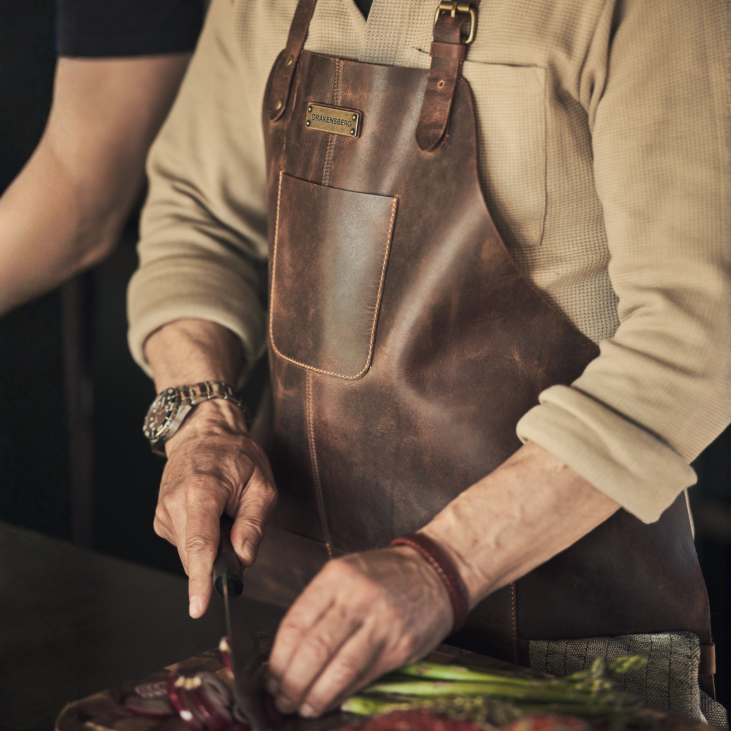 Mann schneidet Ziwebeln in der Küche und trägt eine Ledergrillschürze von DRAKNSBERG in Dunkelbraun Antiklook
