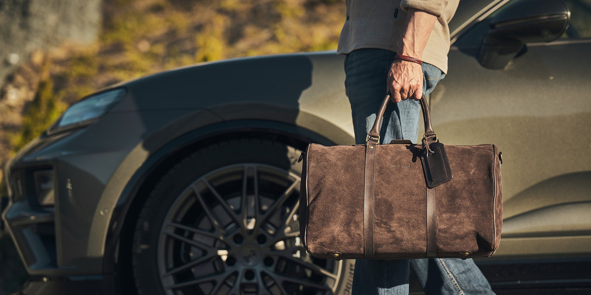 Mann trägt den braunen Veloursleder-Weekender James 50 neben einem Geländewagen