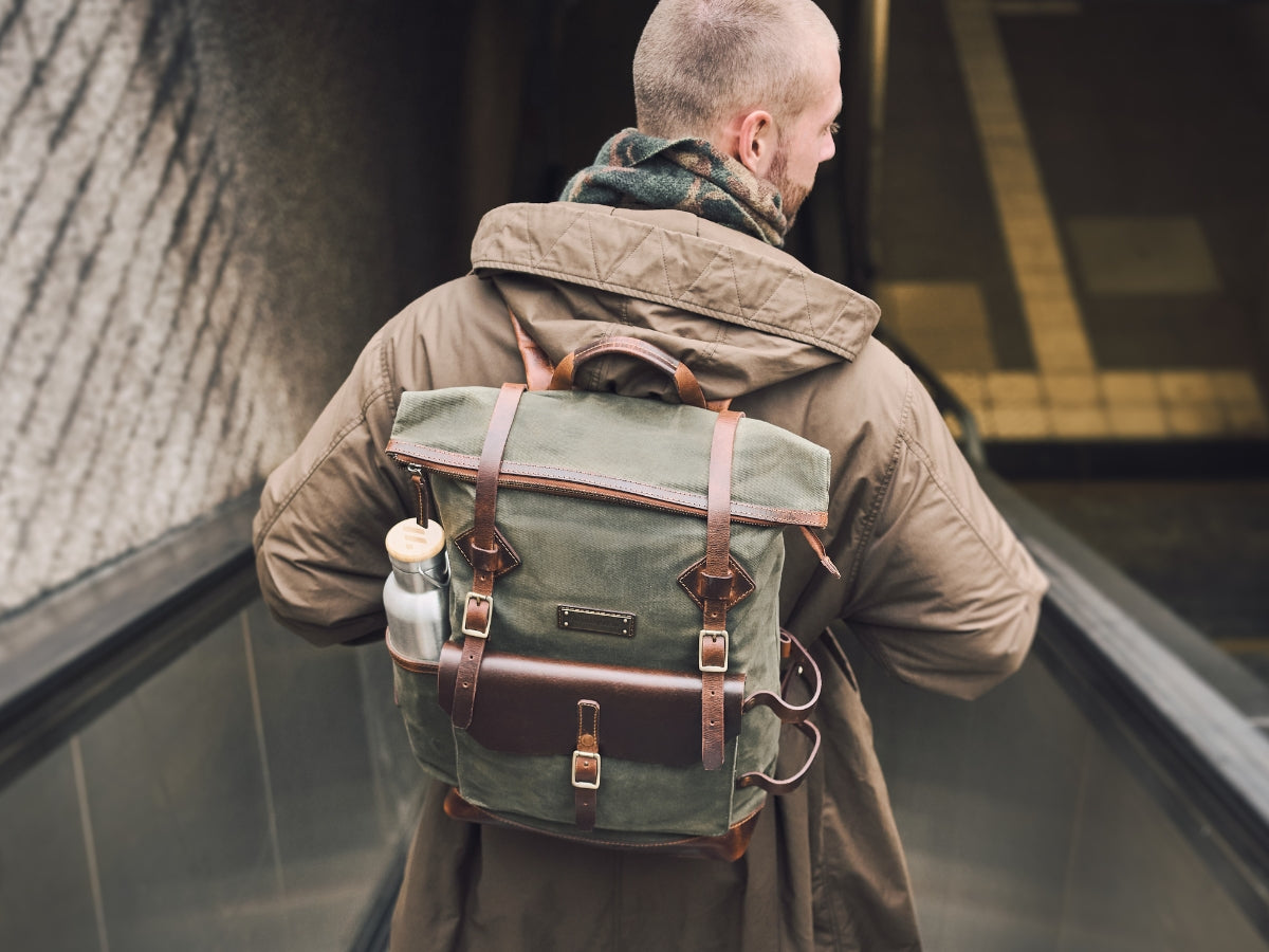 Homme portant un sac à dos en toile verte avec détails en cuir marron