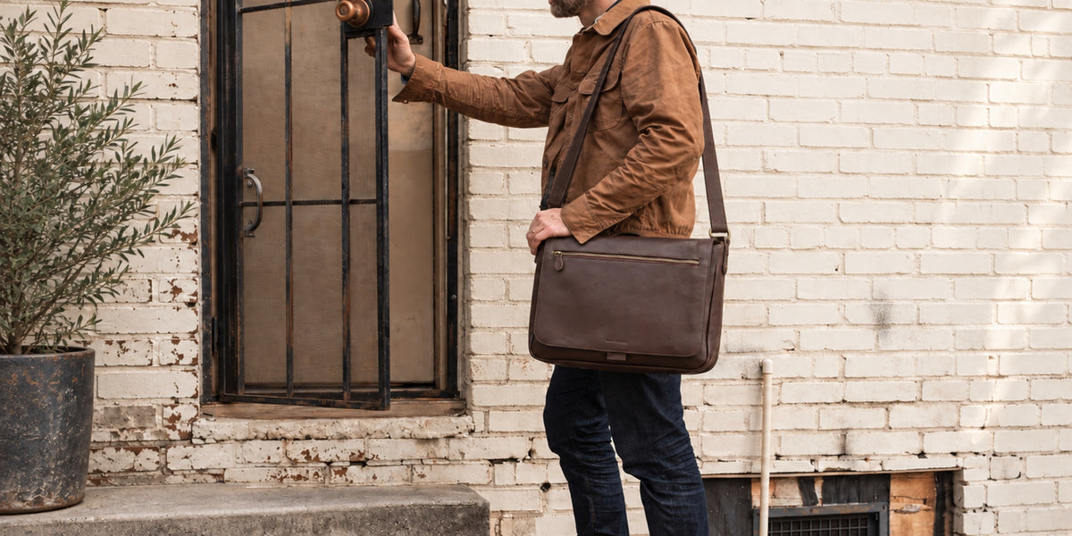 Mann mit der Messenger Bag Leon in Kaffee-Braun vor einer Backsteinfassade