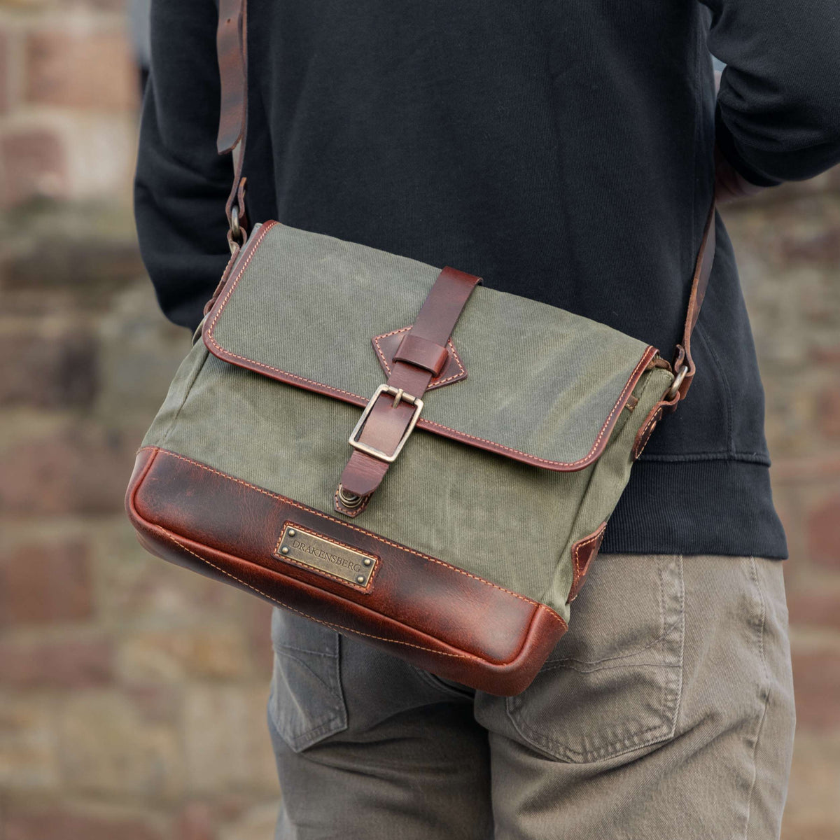 Homme portant le sac bandoulière Nate en toile verte avec une bandoulière en cuir brun