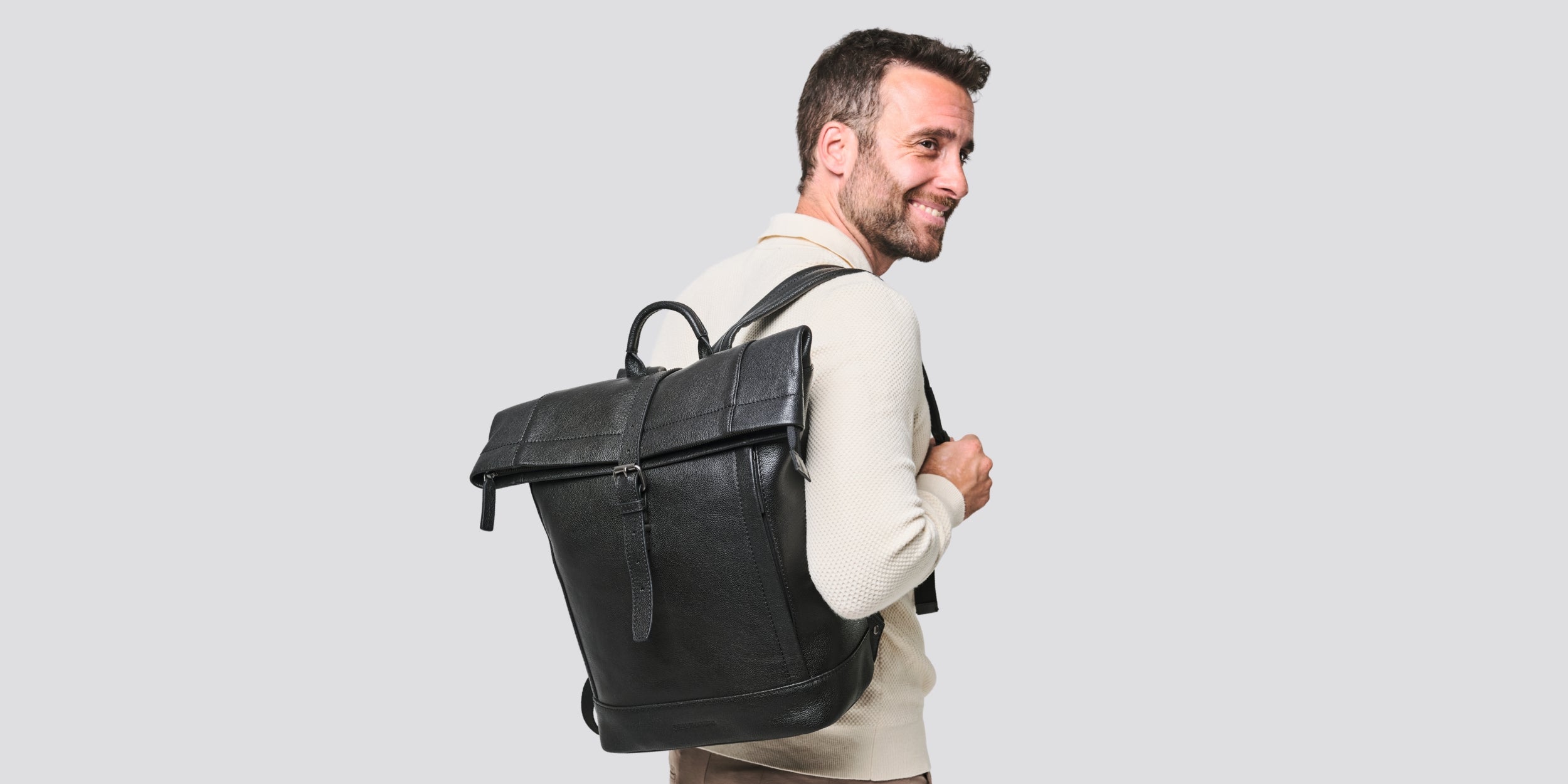 Mann trägt den Rolltop-Rucksack Gino in Schwarz über einem hellen Sakko