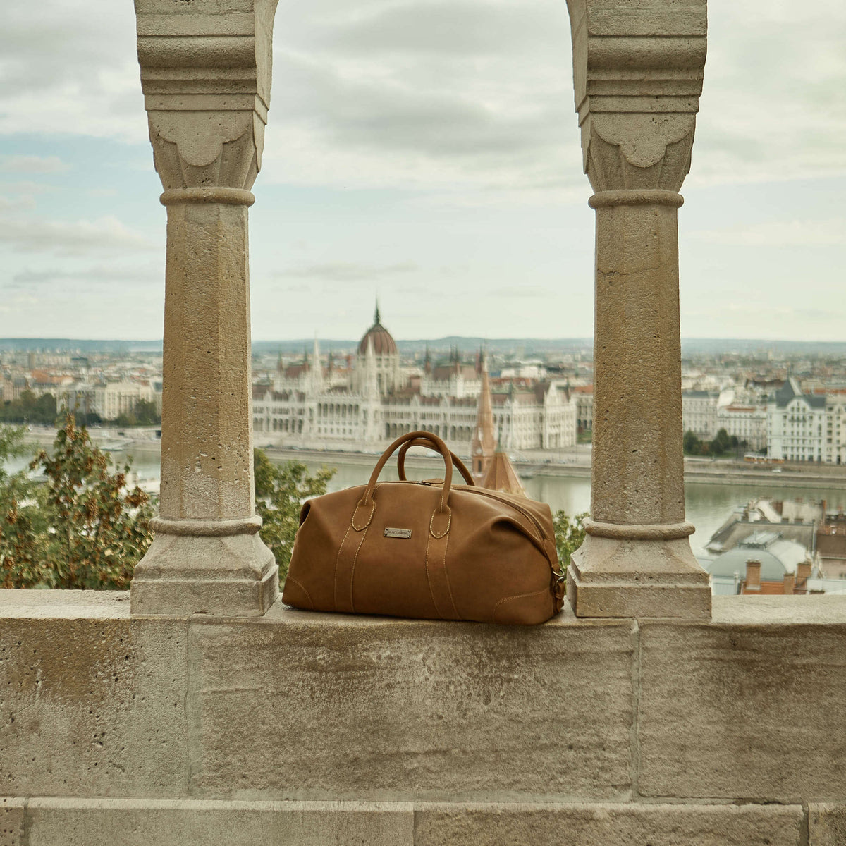 Large David leather weekender in Havana Brown – carried beneath an archway