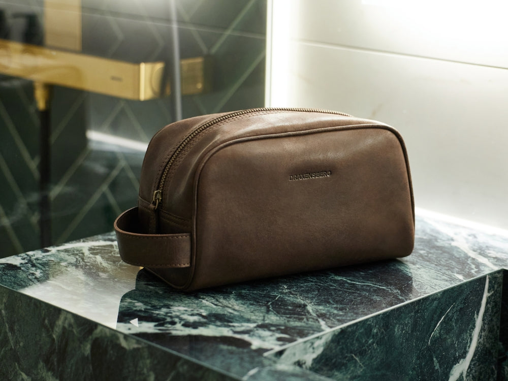 Brown men’s leather wash bag on a marble bathroom shelf