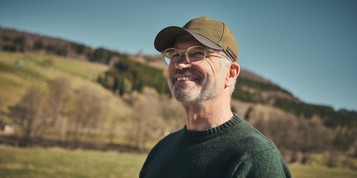 Mann mit Basecap Lennox aus Canvas und Leder in hügeliger Landschaft