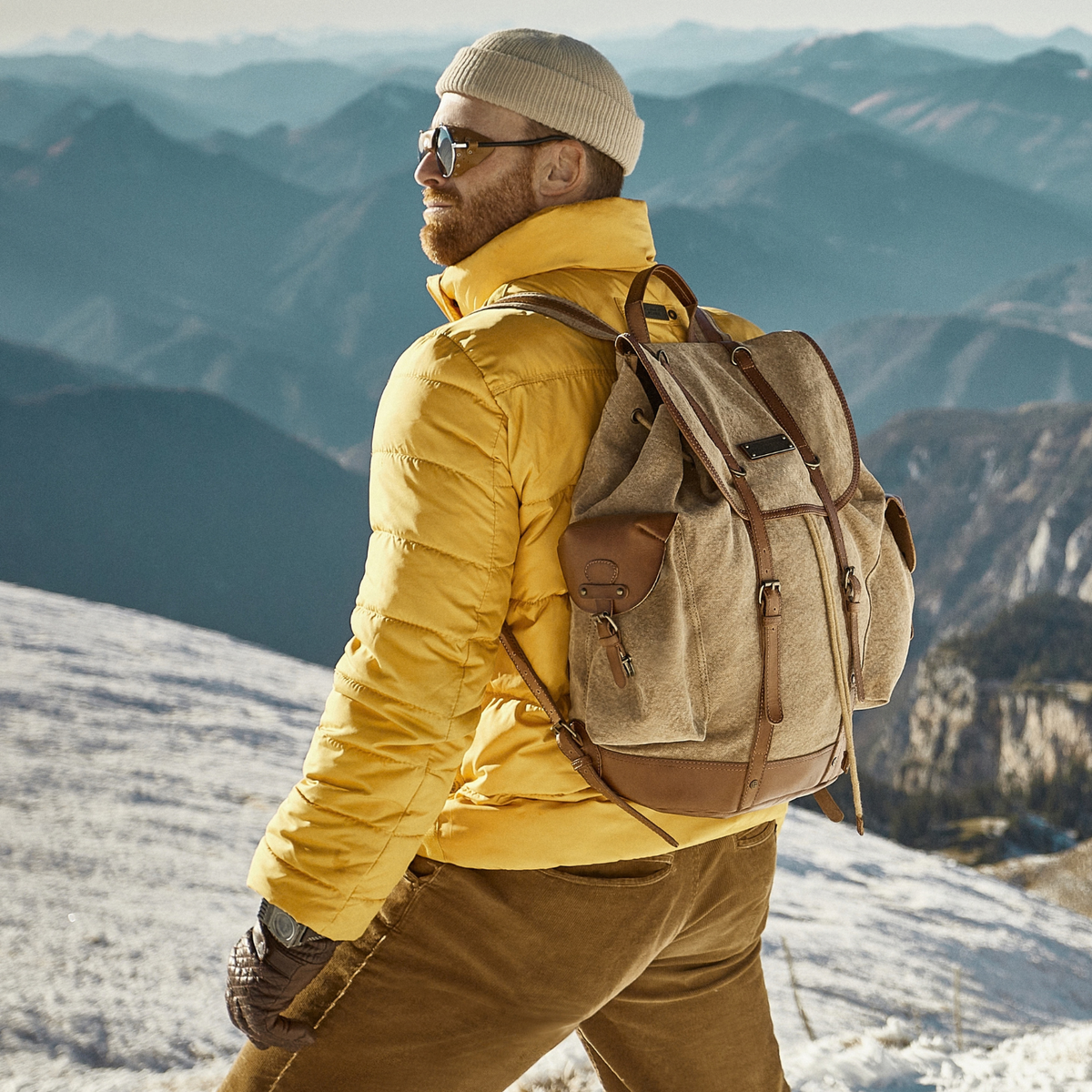 Personne en veste jaune portant un sac à dos Henry devant un panorama montagneux.