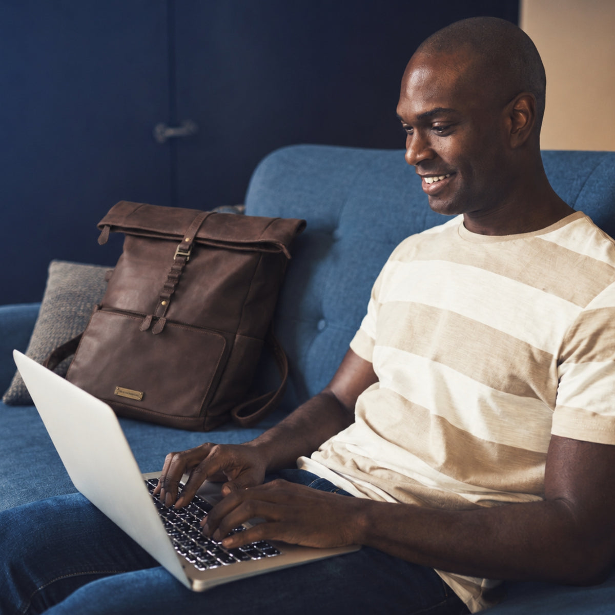 Mann arbeitet am Laptop auf einem Sofa neben dem Reiserucksack Arthur