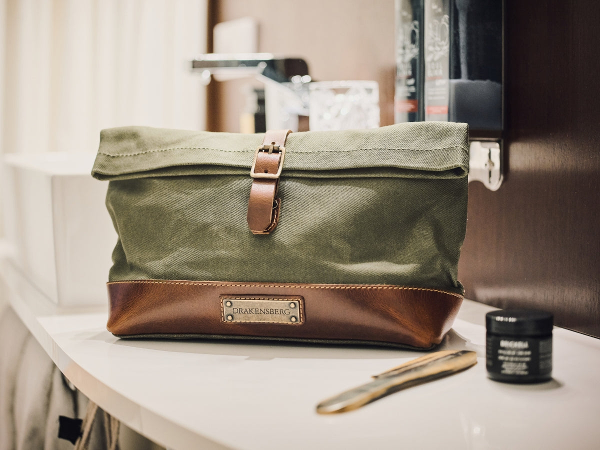 Trousse de toilette en toile vert olive avec fermeture roulée et détails en cuir marron près d’un lavabo
