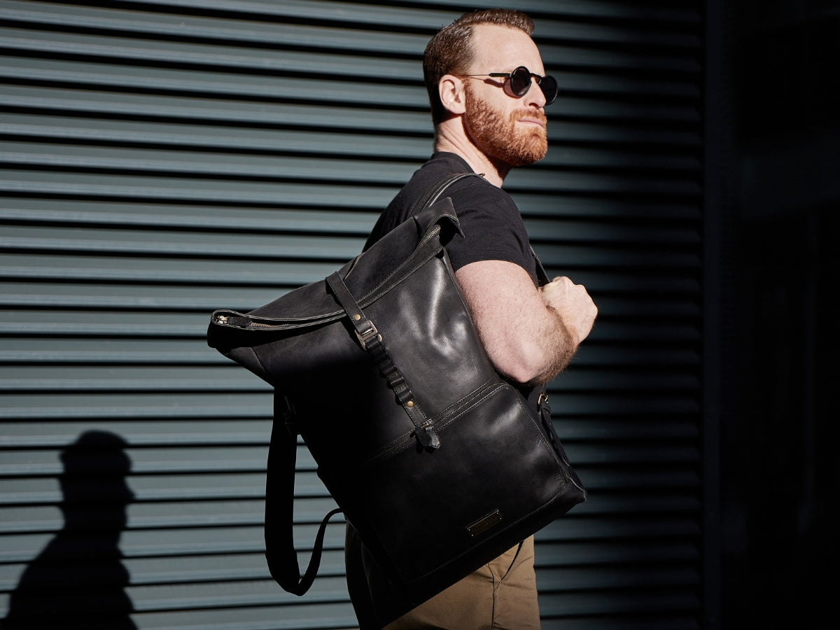 Homme portant un sac à dos rolltop en cuir noir devant une façade en ville