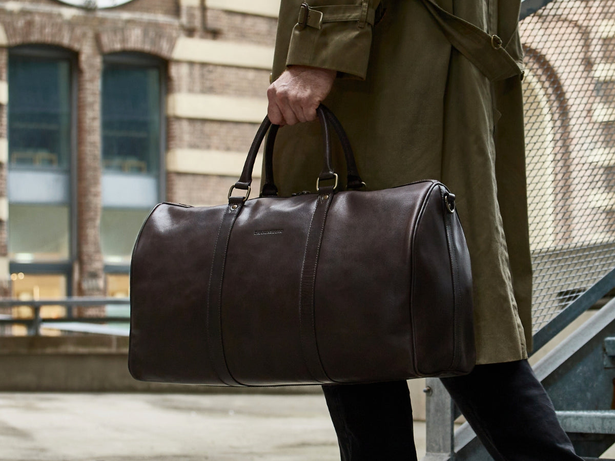 Traveller carrying a dark brown leather weekender by its handles