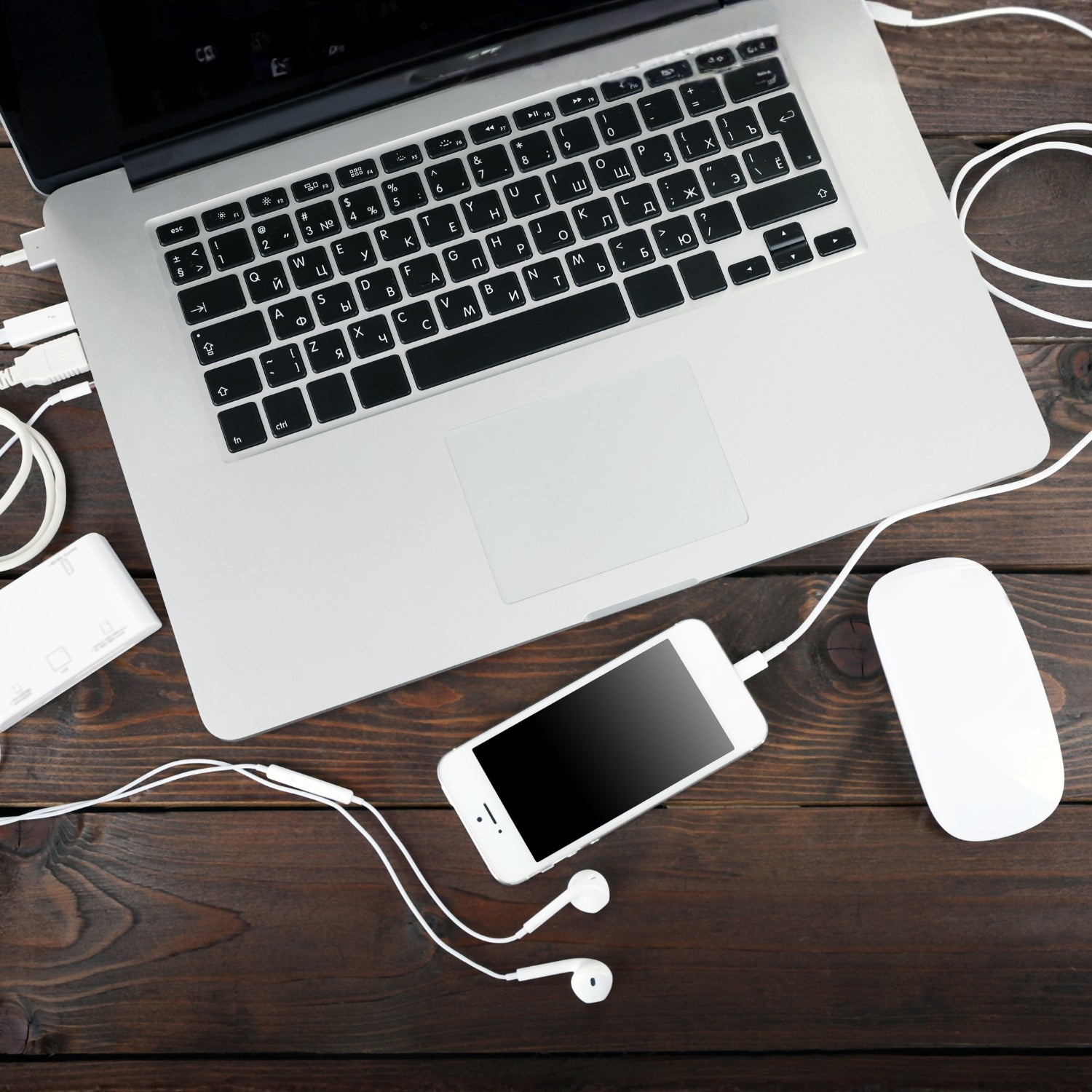 Laptop, Smartphone, Maus, Kopfhörer und Ladekabel auf einem Schreibtisch
