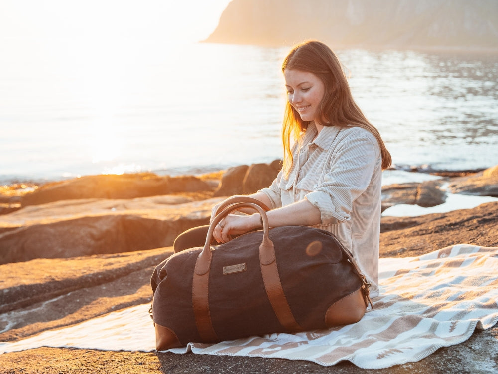 Woman with a brown weekender on a blanket by a rocky coast