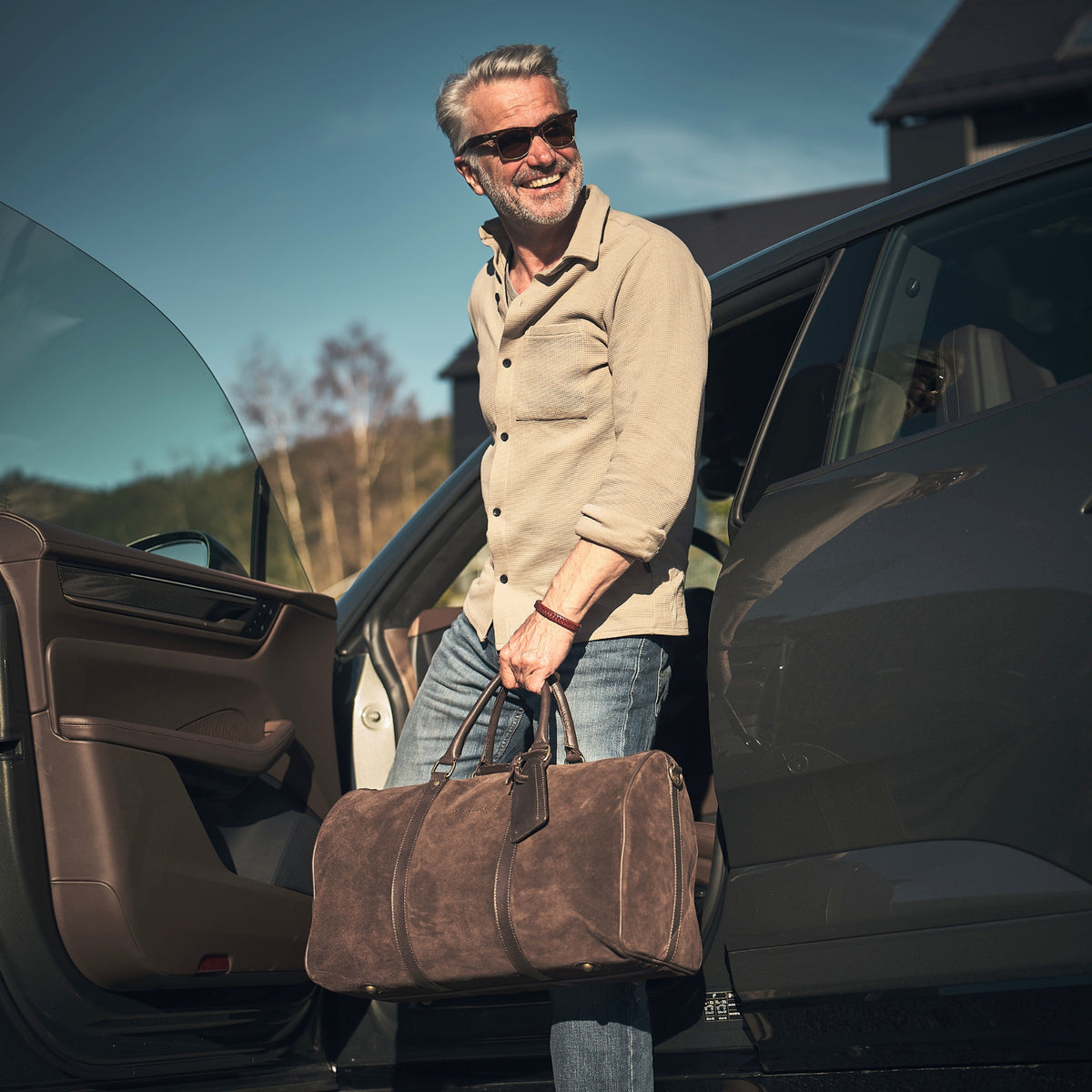 Mann trägt den braunen Veloursleder-Weekender James 50 neben einem SUV